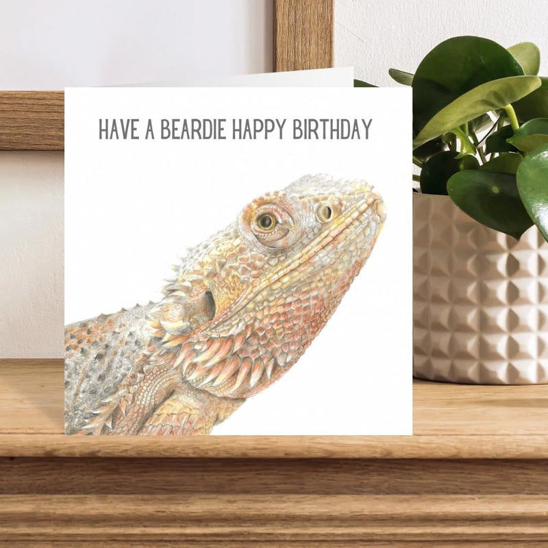 Birthday card with a bearded dragon illustration and text 'Have a beardie happy birthday' on a wooden surface.