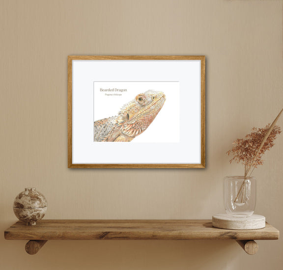 Framed artwork of a bearded dragon on a wall above a wooden shelf with decorative items.
