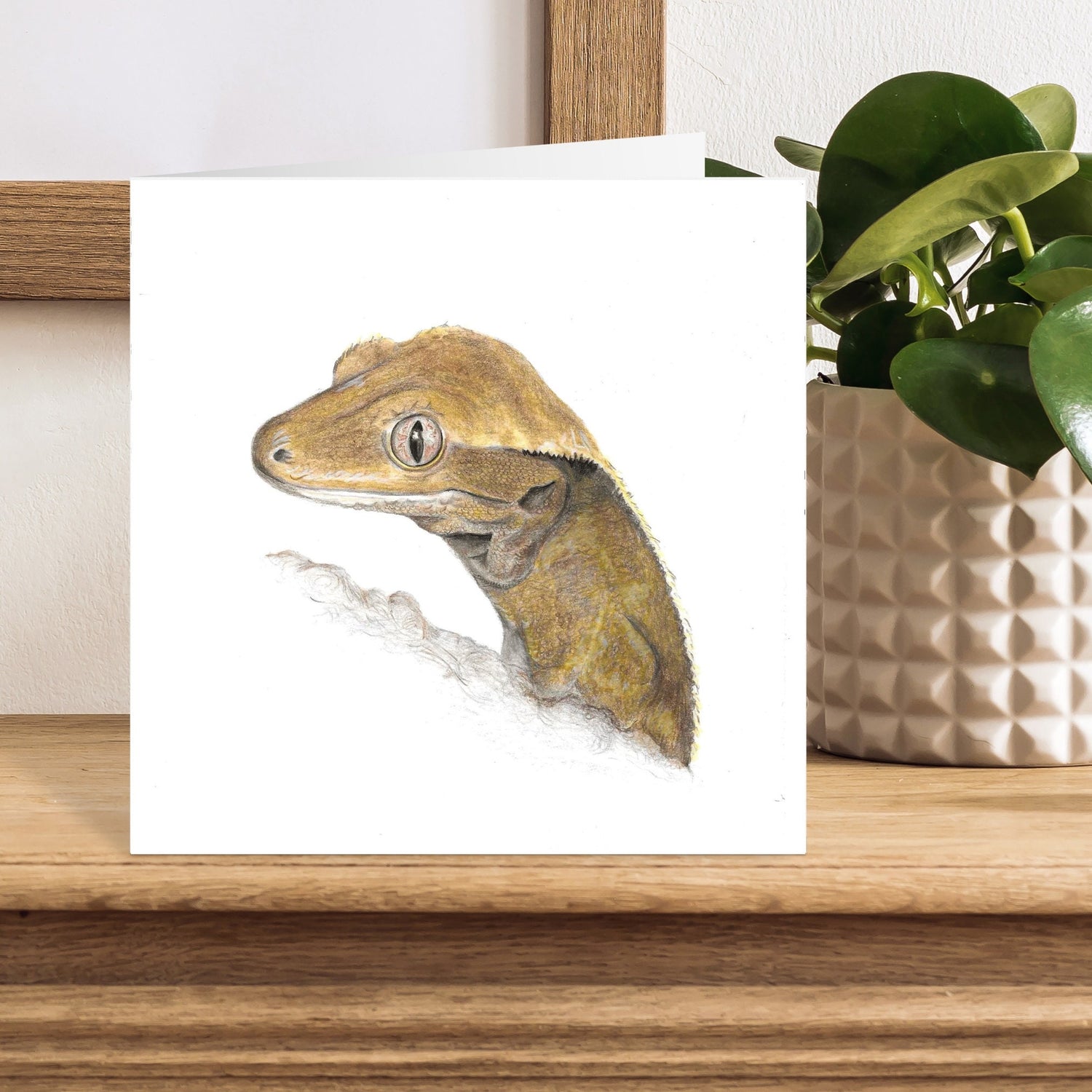 Card with a lizard illustration on a wooden surface with a plant in the background
