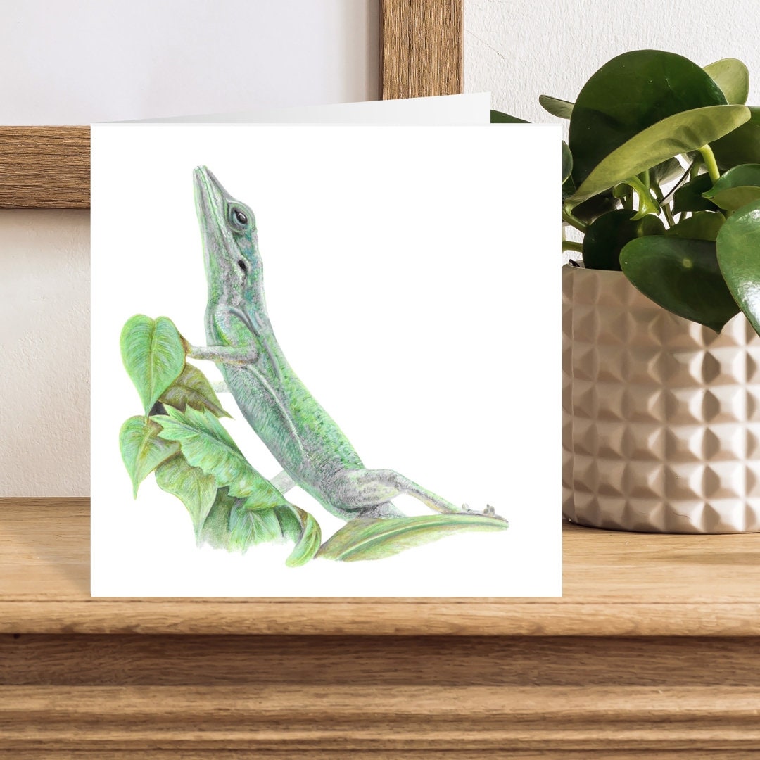 Greeting card with a green lizard colour pencil illustration on a wooden surface with a plant in the background