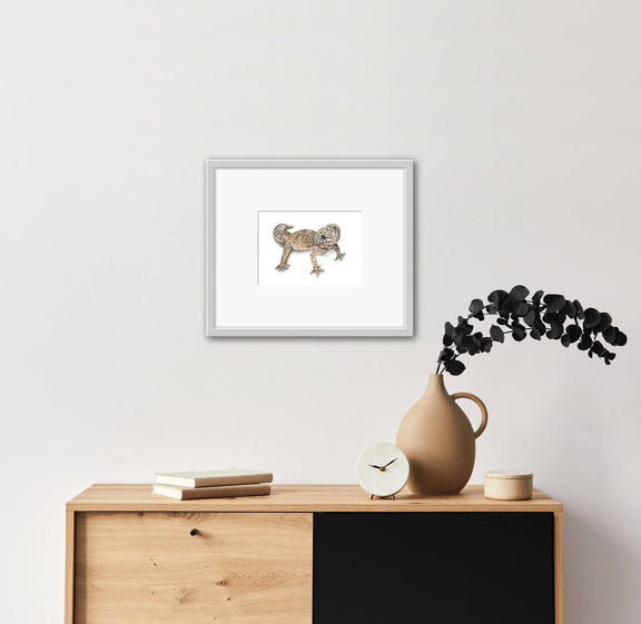 Framed artwork of a Leopard Gecko on a wall above a wooden cabinet with decor items.