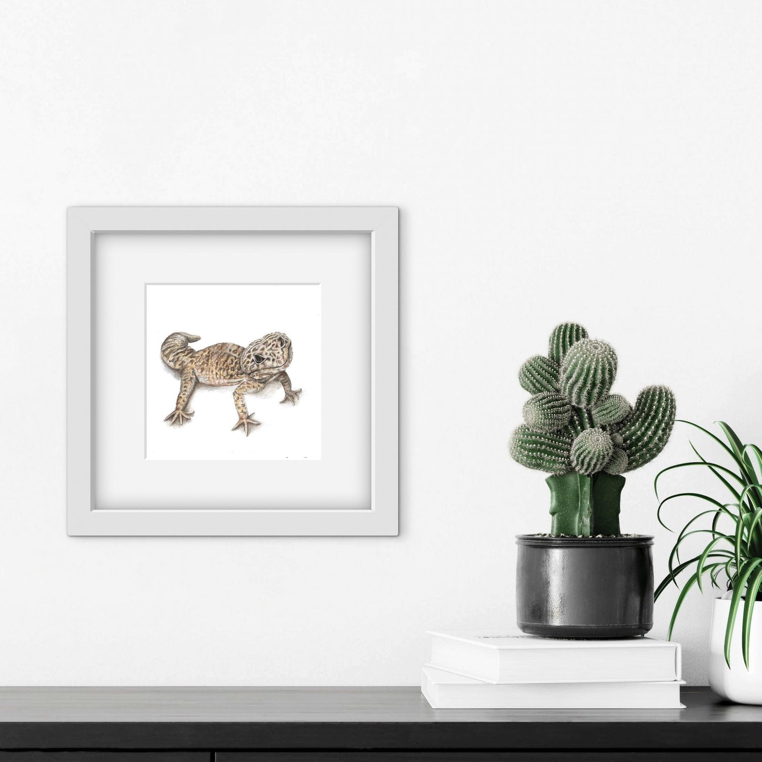 Framed artwork of a Leopard Gecko lizard next to a potted cactus on a white surface