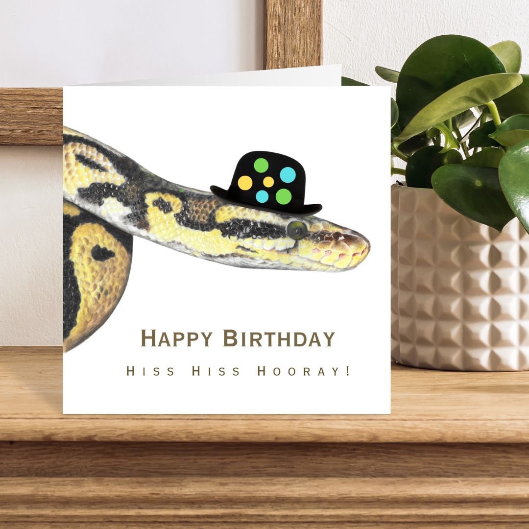 Birthday card with snake wearing a bowler hat on a wooden surface with a plant in the background
