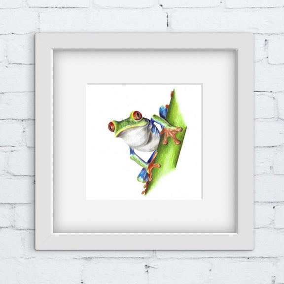 Framed artwork of a colorful frog on a leaf against a white brick wall.
