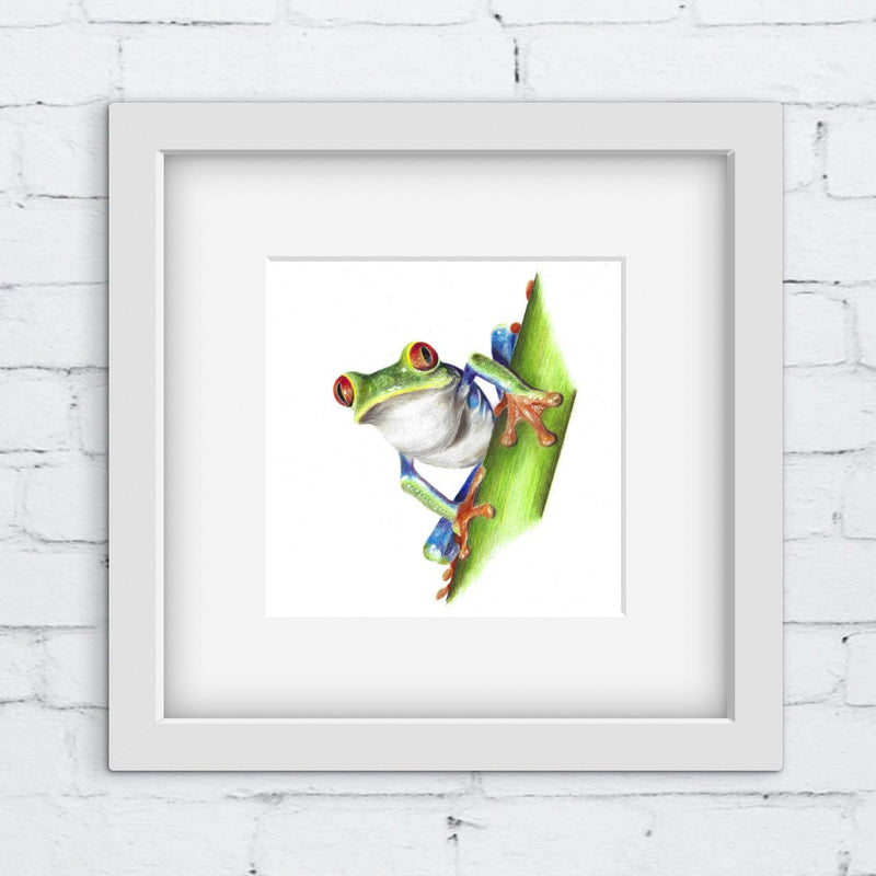 Framed artwork of a colorful frog on a leaf against a white brick wall.