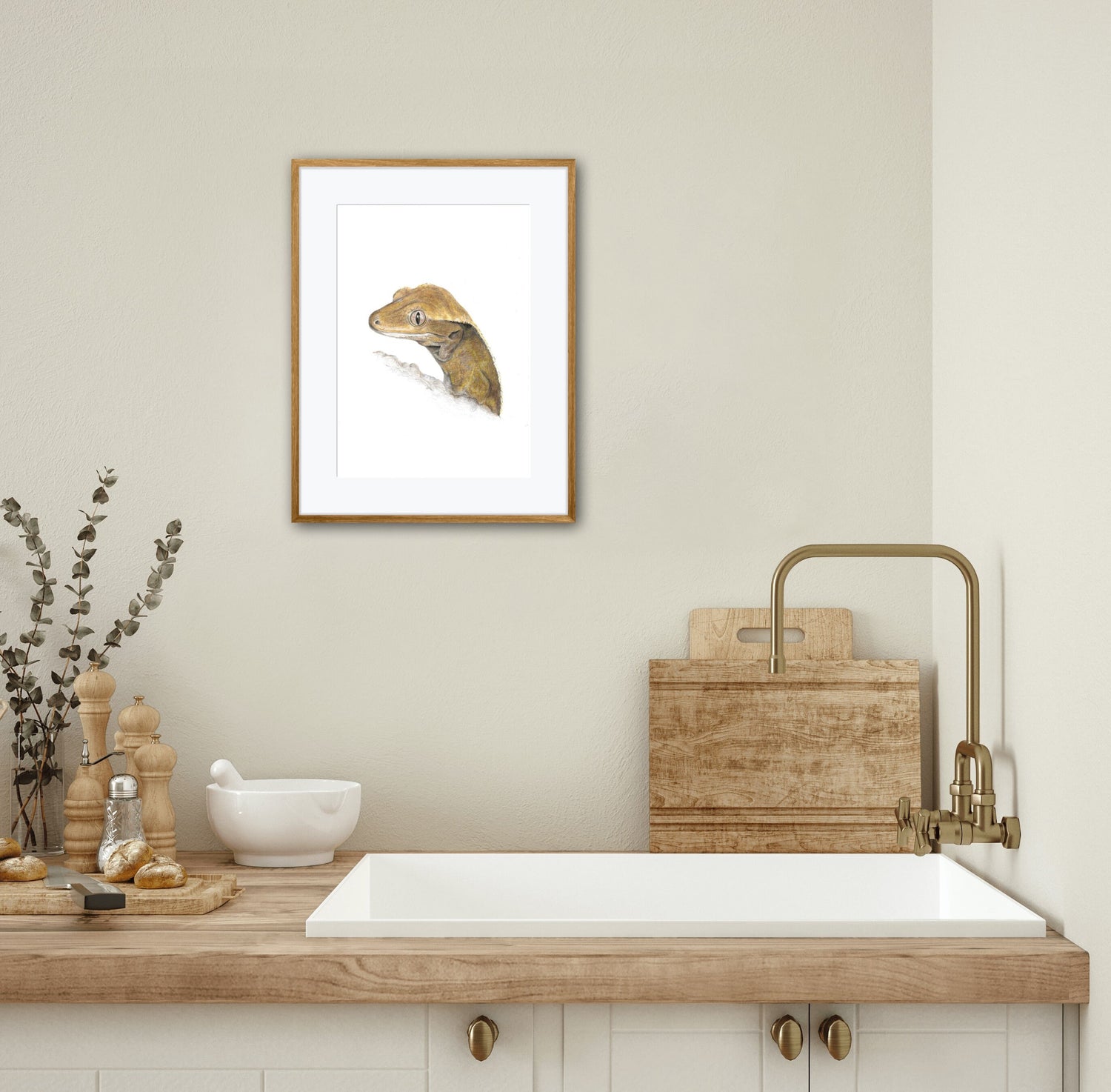 Framed artwork of a crested gecko lizard on a wall above a wooden countertop with a sink.