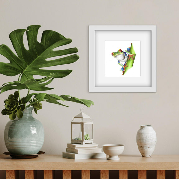 Framed colourful frog artwork on a wall with decorative items on a table below.